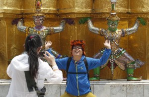 A Chinese tourist strikes a similar pose to statues as they visit the Grand Palace in Bangkok 