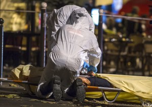 Investigating police officers inspect the lifeless body of a victim of a shooting attack outside the Bataclan concert hall in Paris, France, Saturday, Nov. 14, 2015. Well over 100 people were killed in Paris on Friday night in a series of shooting, explosions. French President Francois Hollande declared a state of emergency and announced that he was closing the country's borders.
