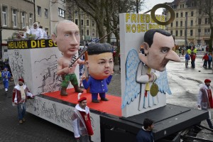 A carnival float depicting from left: Russian president Vladimir Putin, North Korean leader Kim Jong-un and Syrian president Bashar al-Assad as Angels of Peace during the traditional carnival parade in Cologne, western Germany, Monday, Feb. 8, 2016. Many carnival parades in Germany were cancelled because of heavy stormy weather. The foolish street spectacle in Cologne, normally watched by hundreds of thousands of people, is the highlight in Germany's carnival season on Rose Monday. Words on the poster near the Assad doll reads: Nobel Peace Prize. 
