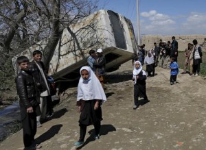 Schoolgirls walk past a damaged mini-bus after it was hit by a bomb blast in the Bagrami district of Kabul, Afghanistan April 11, 2016.