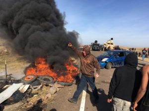 Demonstrators stand next to burning tires as armed soldiers and law enforcement officers assemble on Thursday, Oct. 27, 2016, to force Dakota Access pipeline protesters off private land where they had camped to block construction. The pipeline is to carry oil from western North Dakota through South Dakota and Iowa to an existing pipeline in Patoka, Ill. 