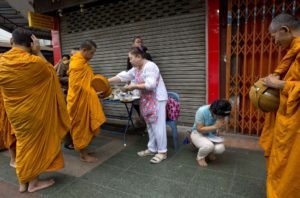 Thai people, some dressed in black, offer alms for Buddhist monks close to Grand Palace in Bangkok, Thailand, Friday, Oct. 14, 2016. Grieving Thais went to work dressed mostly in black Friday morning, just hours after the palace announced the death of their beloved King Bhumibol Adulyadej, the politically fractious country's unifying figure and the world's longest-reigning monarch.