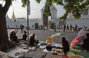 hai people sit in front of Grand Palace, wait for the body of Thailand's King Bhumibol Adulyadej to be carried in Bangkok, Thailand, Friday, Oct. 14, 2016. Grieving Thais went to work dressed mostly in black Friday morning, just hours after the palace announced the death of their beloved King Bhumibol, the politically fractious country's unifying figure and the world's longest-reigning monarch.