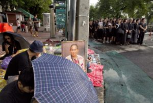 A portrait of Thai King Bhumibol Adulyadej, center is displayed as Thai people stand in lines to offer condolences for the king at Grand Palace in Bangkok, Thailand, Friday, Oct. 14, 2016. Grieving Thais went to work dressed mostly in black Friday morning, just hours after the palace announced the death of their beloved King Bhumibol, the politically fractious country's unifying figure and the world's longest-reigning monarch.