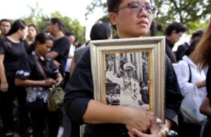 A Thai woman holds on to a portrait of Thai King Bhumibol Adulyadej in a line to offer condolences for the king at Grand Palace in Bangkok, Thailand, Friday, Oct. 14, 2016. Grieving Thais went to work dressed mostly in black Friday morning, just hours after the palace announced the death of their beloved King Bhumibol, the politically fractious country's unifying figure and the world's longest-reigning monarch.