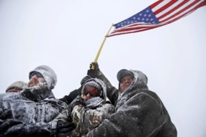 Military veterans huddle together to hold a United States flag against strong winds during a march to a closed bridge outside the Oceti Sakowin camp where people have gathered to protest the Dakota Access oil pipeline in Cannon Ball, N.D., Monday, Dec. 5, 2016. 